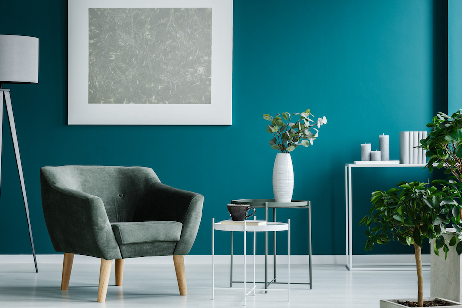 Green armchair against blue wall with silver painting in living room interior with plants